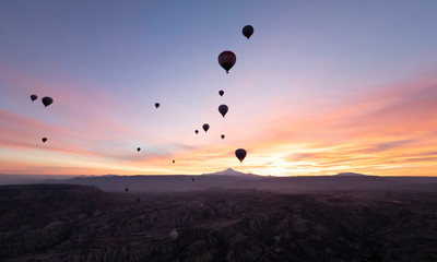 View of a volcano Mount Kayseri and silhouette of balloons seen from Goreme, Cappadocia with beautiful sunrise and colourful, golden, orange, pink and blue sky. It's fun, excited and impress activity 