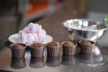 Homemade 5 chocolate capcakes ready to decorate. Selected focus with blurred bowl and plate of meringues at the background. Home baking consept.