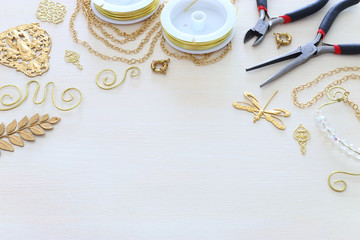 Jewellery making concept with gold chain, filigree charms and tools over white wooden background