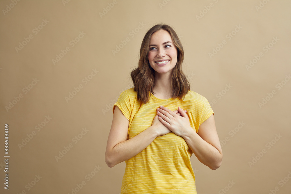 Wall mural Beautiful girl holding her hands on her heart showing how much she care and love 