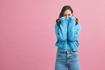 Portrait of happy and lovely young woman in a blue winter sweater on a pink background