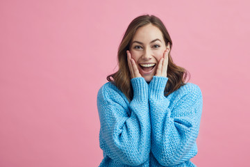 Excited beautiful girl holding her hands against her cheeks, while having a nice sweater on that...