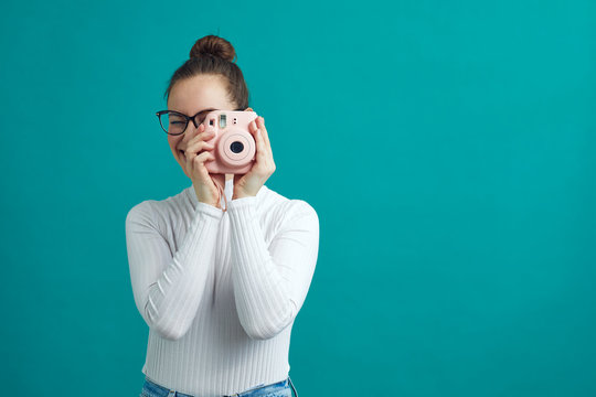 Young woman taking a photo with a polaroid camera, while standing on a nice color background