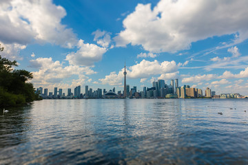 The skyline of Toronto, a view from the lake side - Toronto, Ontario, Canada. Panorama view of the Canadian city of Toronto, with white clouds on a blue sky with the Toronto tower. Urban view of city