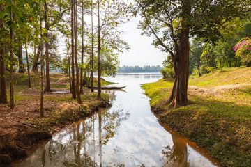 Traditional long tail wooden boat in a small lake near Siem Reap, Cambodia. The sky and the trees around is reflected in the water. Idyllic place just near the most visited place of Cambodia