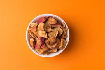 Homemade dried fruit apple chips in a white bowl on a orange background. Organic natural wholesome food.
