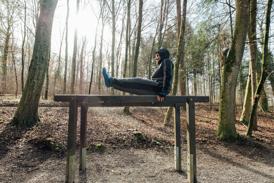 Young man exercising on wooden parallel bars outdoors