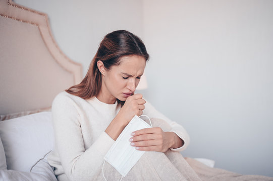 Coronavirus disease (COVID-19) symptoms - runny nose, sore throat, cough, fever. Young woman with face mask sick of flu viral infection spreading corona virus lying in bed at home quarantine isolation
