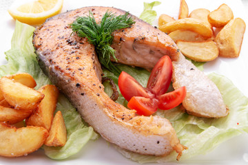 A dinner of fried fish, chips, french fries, served with a fresh salad , tomato and a the piece of lemon