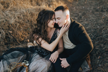 Loving groom in a black cardigan and a cute bride in an expensive dress are hugging, sitting in the...
