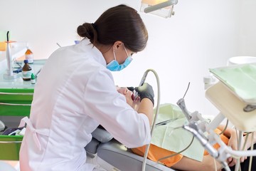 Woman doctor dentist treating teeth to girl patient in dental office