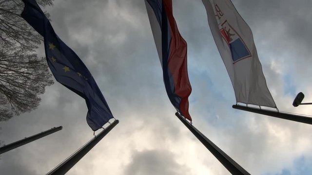 Slow motion looking up rotating European, Slovenian and State Protocol Services of Slovenia flags waving in wind