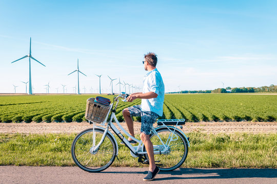 young man electric green bike bicycle by windmill farm , windmills isolated on a beautiful bright day Netherlands Flevoland Noordoostpolder