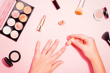 How to get perfect manicure at home concept. Woman doing herself a manicure with makeup items and tools around on pink background. Pastel table top, beauty flat lay with female hands