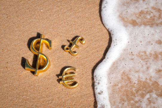 Golden three-dimensional symbols of international dollar, euro and pound currency with wave encroaching on the sand of an empty sunny beach