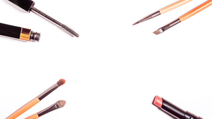 Flat lay with make up products in minimal style on white desk. Frame with black mascara, lipstick, spring eyeshadow palette, different make up brushes. Top view, copy space.