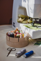 White sewing machine and colorful threads with needles and measuring tape with green textile background