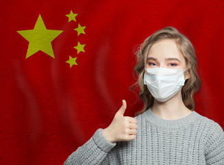 Happy woman in face mask holding thumb up on national flag China. Flu epidemic and virus protection...