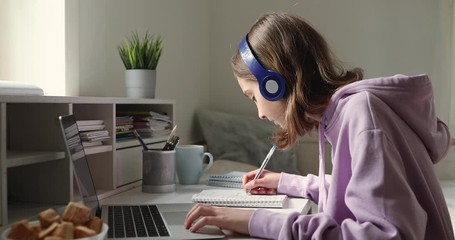 Teenage girl wearing headphones studying online from home with distance teacher. Teen school student distance learning in internet making notes, doing homework, watching video tutorial course concept. - Powered by Adobe