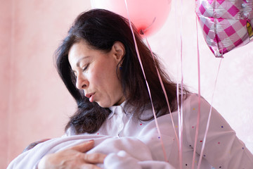 Young grandmother holding baby sitting on bed. Young beautiful grandmother spends time with newborn...
