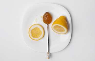 Sliced ​​Lemon and a spoon of honey on a white plate