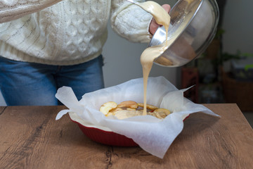 The hostess prepares apple charlotte at home in the kitchen and pours the dough into a baking dish