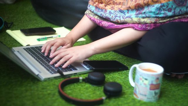 Young Indian woman with a colorful kashmiri shawl typing on a laptop sitting cross legged on grass