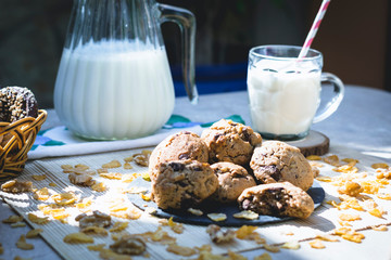 Plate with chocolate chip cookies, with glass of milk and milk jug in the background on woody table...