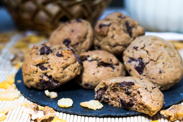 Plate with chocolate chip cookies with baskets of sweets in the background and cereals scattered on the table