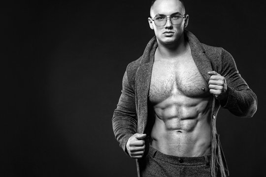 Portrait of handsome stylish man bodybuilder with naked torso in elegant suit. Guy in glasses. Black and white photo
