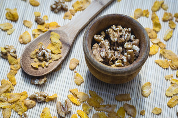 Bowl with nuts next to a spoon with cereals on a wooden background with scattered cereals