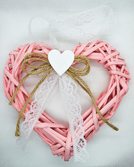 Wicker pink heart with a white lace bow on a white background