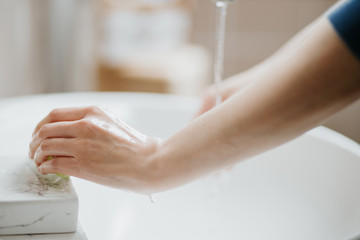 Closeup of a woman washing her hands in bathroom to prevent Covid-19 viral infection. Recommended washing with soap and running water during coronavirus pandemic.