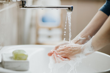 Closeup of a woman washing her hands in bathroom to prevent Covid-19 viral infection. Recommended washing with soap and running water during coronavirus pandemic. - Powered by Adobe