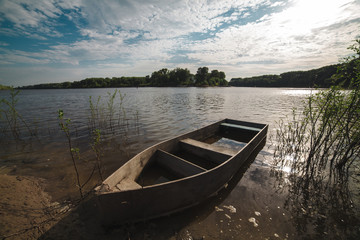 Old wooden fishing boat near the river bank, blue sky with clouds on the background