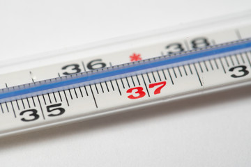 Mercury in glass thermometer on white surface. Copy space on top and bottom. Fever thermometer in analog form for measuring high temperature due to illness like flu or coronavirus