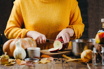 Close-up photo of woman's hands in yellow sweater cutting apples for hot wine. Winter cozy holidays mood.