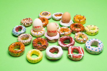 Easter concept. Collection of decorative handmade ceramic doughnuts / donuts and easter eggs on apple green background, close up.