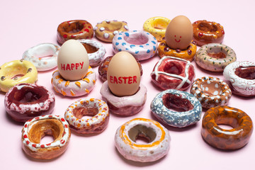 Easter concept. Collection of decorative handmade ceramic doughnuts / donuts and easter eggs on apple pink background, close up.
