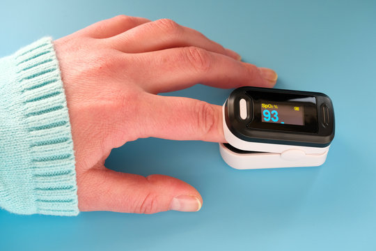 Pulse Oximeter portable digital device to measure person's oxygen saturation. Reduction in oxygenation is an emergency sign of Covid-19 viral pneumonia. Device on female hand, blue mint background.