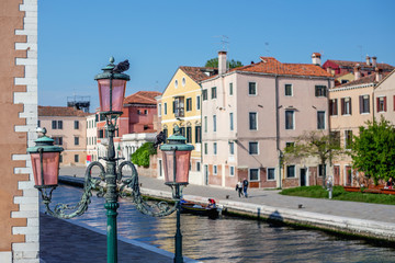 Old vintage street lamp covered with patina on the background of a beautiful river of blue color and colorful houses.