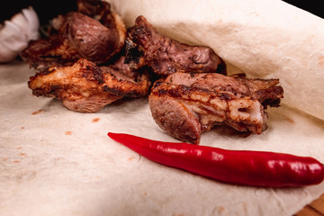 Appetizing fried meat lies on a wooden tray, among the seasonings. Studio photography of food in the cooking industry, dark background