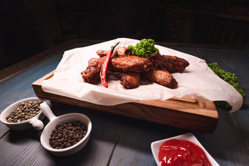 Appetizing fried chicken wings on a wooden tray. Studio photography of food in the cooking industry, dark background