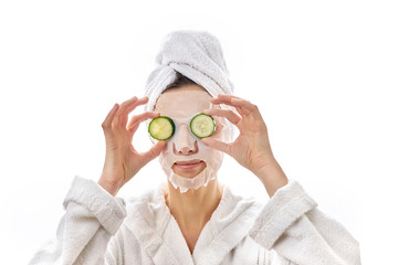 A woman with a face mask and a slice of cucumber smoothes them to her eyes. Skin tone around the eyes. Mature beautiful clean skin. Isolated white background.