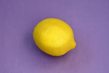 Bright yellow lemon on a purple background close up