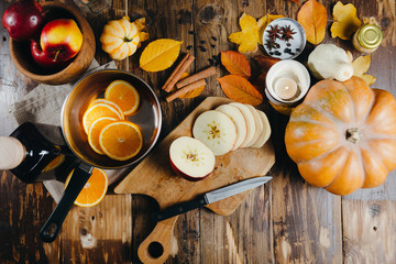 Flatlay with ingredients for cooking mulled wine. Cutted apples on a wooden board, oranges, cinnamon sticks, anise stars, cardamon, pimpkins and candles.