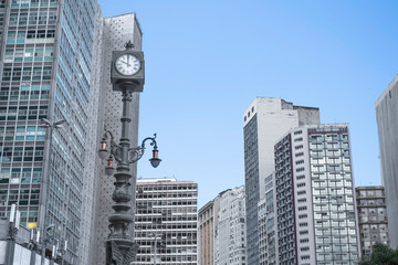 Vintage street clock on the background of high-rise buildings and office buildings in a big city. Skyscrapers on the background of blue sky.