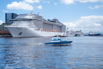 Speedboat, big white ocean cruise liner and cargo ship in the port against the background of blue...