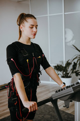 Side view of fit woman exercising on electro muscular machine.