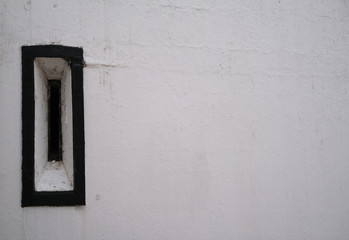 One old antique window with a black frame with flaky paint on a white stone wall.